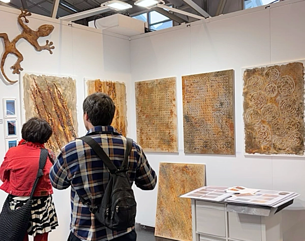 Besucher der Kunstmesse artfair in Frankfurt betrachten rostfarbene Reliefbilder und moderne Metallkuns. Die ausgestellten Werke zeigen abstrakte Strukturen und texturierte Oberflächen im Industrial- und Rost-Design.