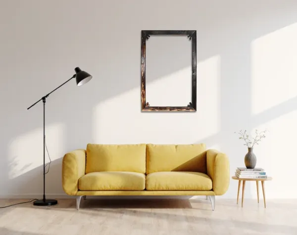 Das Bild zeigt ein Wohnzimmer mit einem gelben Sofa, einem leeren, verkohlten Bilderrahmen, einer Stehlampe und einem kleinen Beistelltisch mit Vasen und Büchern. Sonnenlicht fällt durch ein Fenster.