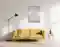 Das Bild zeigt ein Wohnzimmer mit einem gelben Sofa, einer Stehlampe und einem abstrakten Wandbild mit durchsichtiger Folie. Auf einem Beistelltisch stehen eine Vase mit Pflanzen und Bücher.