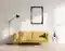 Das Bild zeigt ein Wohnzimmer mit einem gelben Sofa, einem leeren, verkohlten Bilderrahmen, einer Stehlampe und einem kleinen Beistelltisch mit Vasen und Büchern. Sonnenlicht fällt durch ein Fenster.